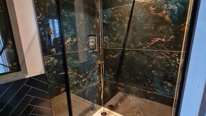 A modern bathroom with a glass-enclosed shower, marble walls, and a black tiled floor.