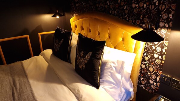 Una cama con cabecera capitonada, una lámpara de noche y una pared con diseños de corazones y llaves.