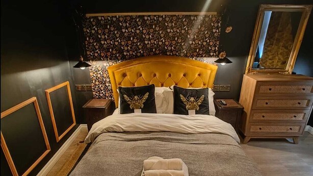 A neatly made bed with a headboard, a bedside table with a lamp, a dresser, and a mirror.