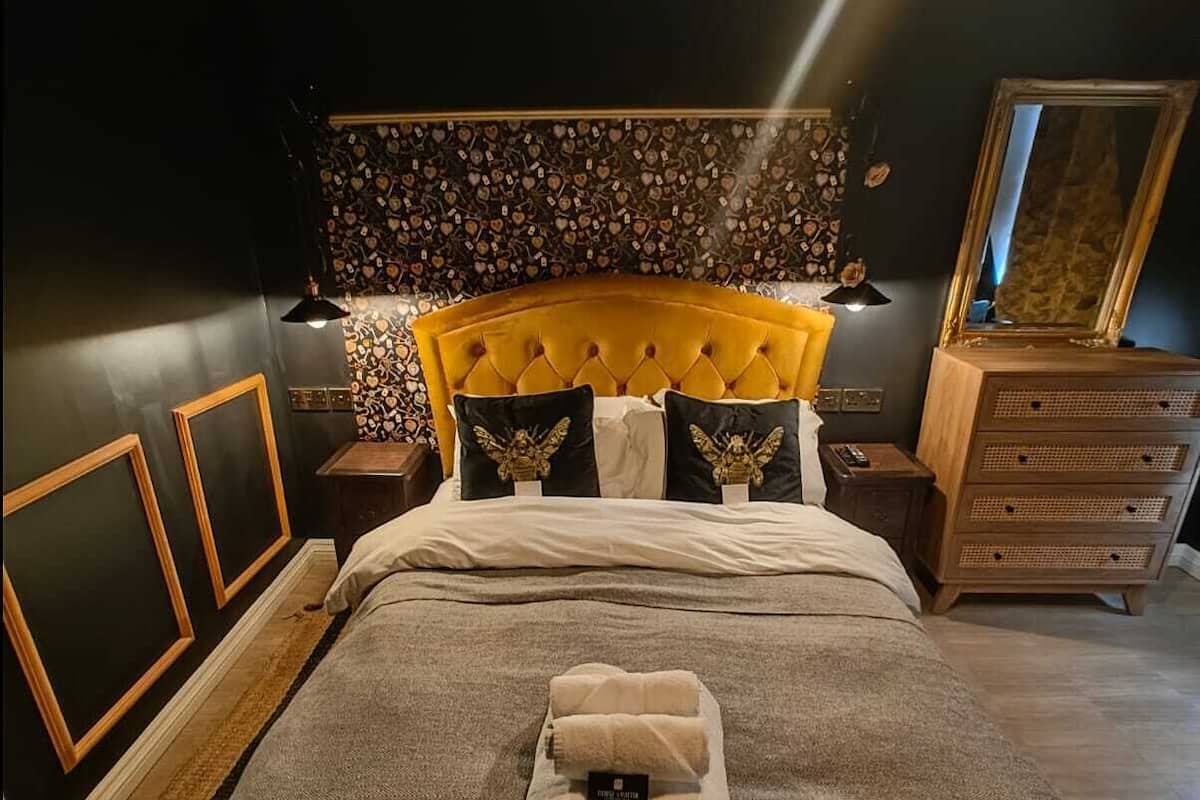 A neatly made bed with a headboard, a bedside table with a lamp, a dresser, and a mirror.