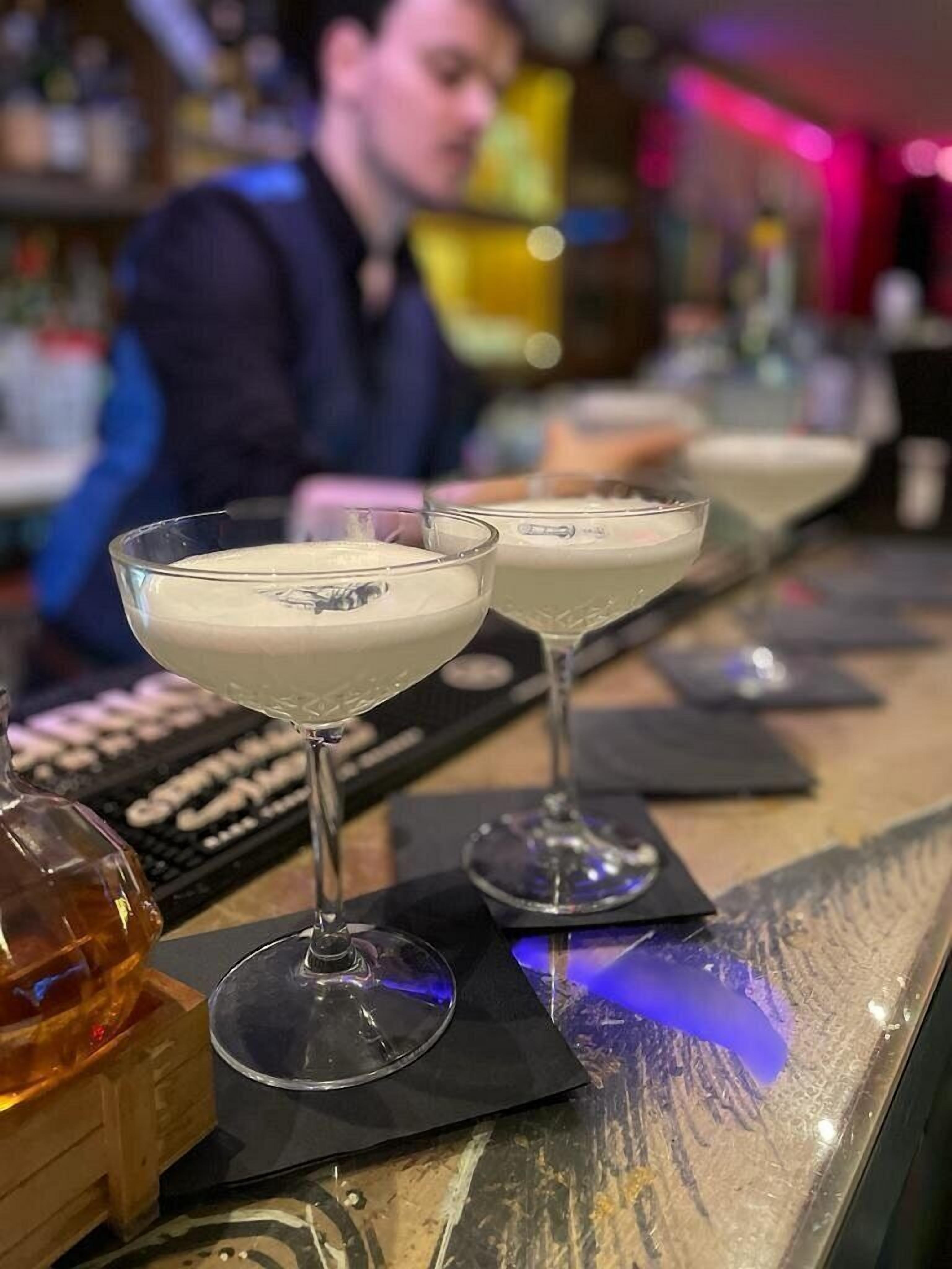 Three glasses of a creamy beverage on a bar counter with a keyboard and a bottle in the foreground.