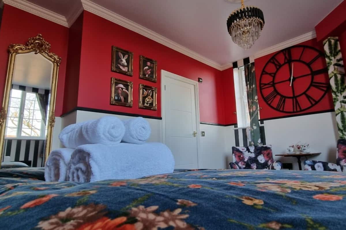 A room with a bed, a large clock, and a mirror.