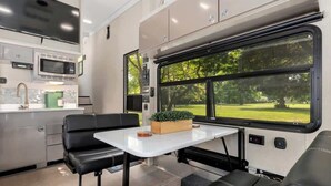 A compact RV kitchen with a microwave, sink, and a small dining area with a table and chairs.