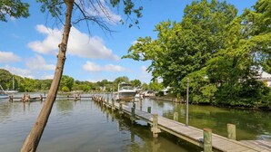 A calm river with a wooden dock extending into the water, surrounded by lush greenery and boats.
