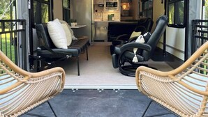 A cozy interior with two black leather sofas, a small coffee table, and wicker chairs. A flat-screen TV is mounted above the seating area.