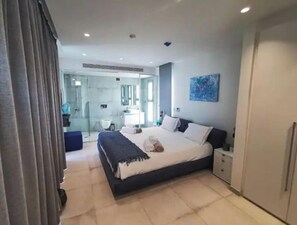 A modern bedroom with a large bed, bedside tables, a wardrobe, and a bathroom visible through a glass door.