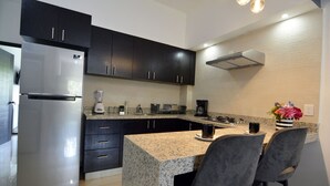 A modern kitchen with dark cabinets, a stainless steel refrigerator, granite countertops, a built-in stove, and a small dining area with two chairs.