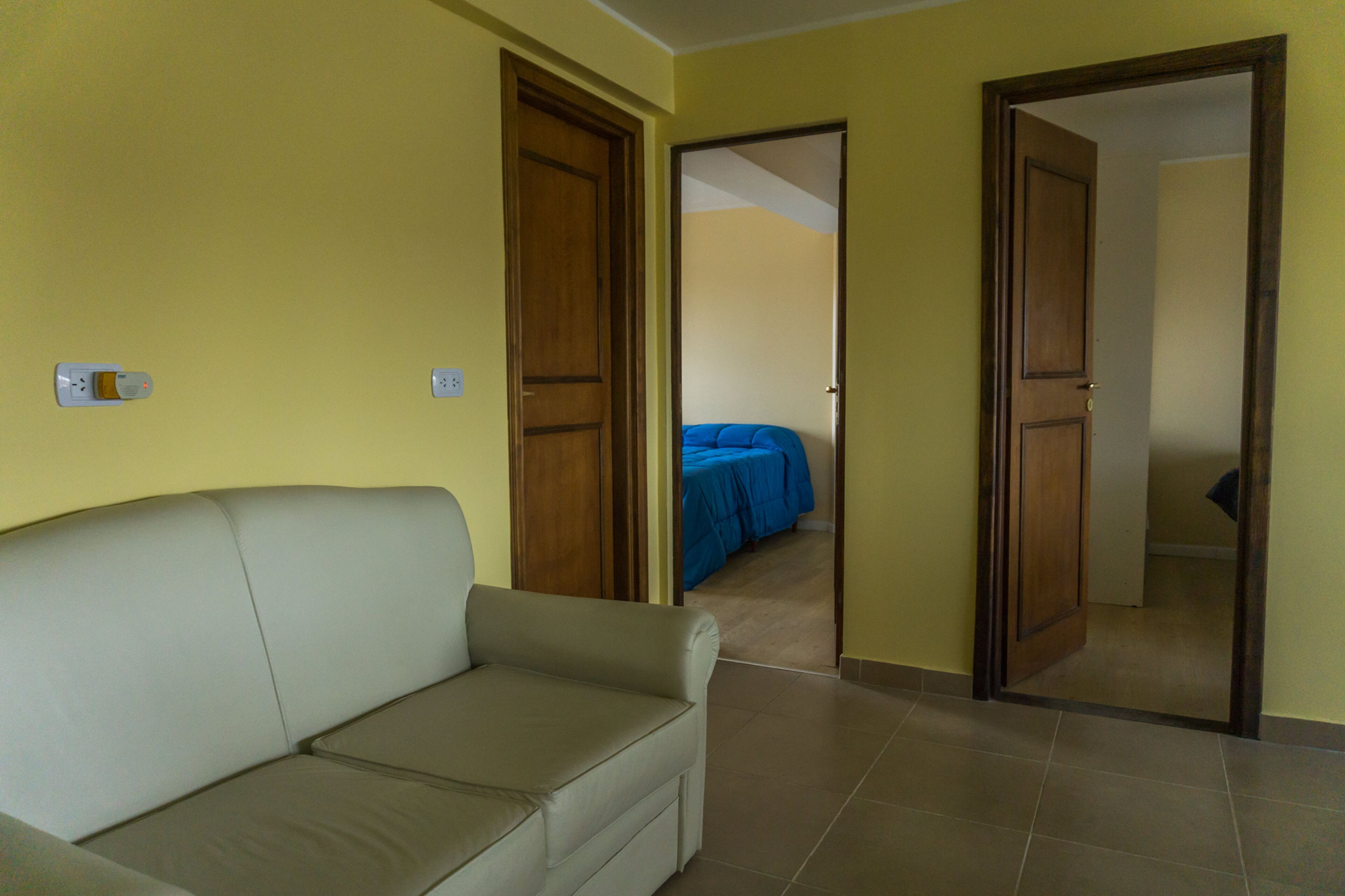 Habitació amb un sofà, un llit amb roba de llit blava i portes de fusta.