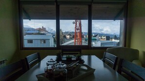 A dining table with chairs, a window with a view of buildings and mountains, and a tray with jars and utensils. - Gente del Sur - Odino (Ushuaia)