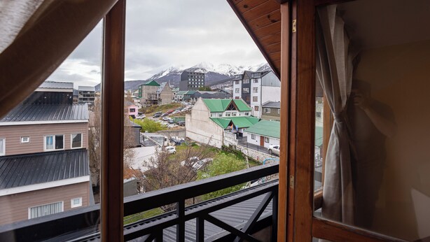 A view from a window with a wooden frame, overlooking a town with buildings and mountains in the background. - Gente del Sur - Odino (Ushuaia)