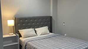 A modern bedroom with a grey bed, a bedside table with a lamp, a built-in air conditioning unit, and a grey wall. - A beautiful Studio all inclusive (Allentown)