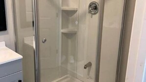 A corner shower enclosure with a glass door, a control panel, and a small shelf inside. - A beautiful Studio all inclusive (Allentown)