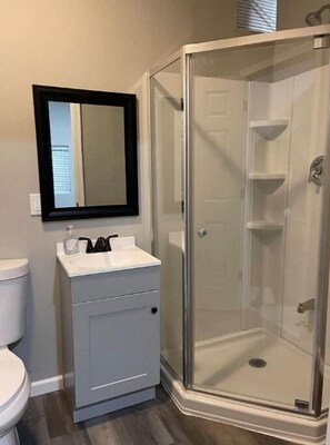 A bathroom with a toilet, a sink with a mirror, and a glass-enclosed shower.