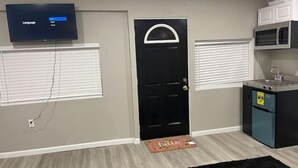 A compact kitchen with a black door, a television mounted above the door, and a microwave above the sink. - A beautiful Studio all inclusive (Allentown)
