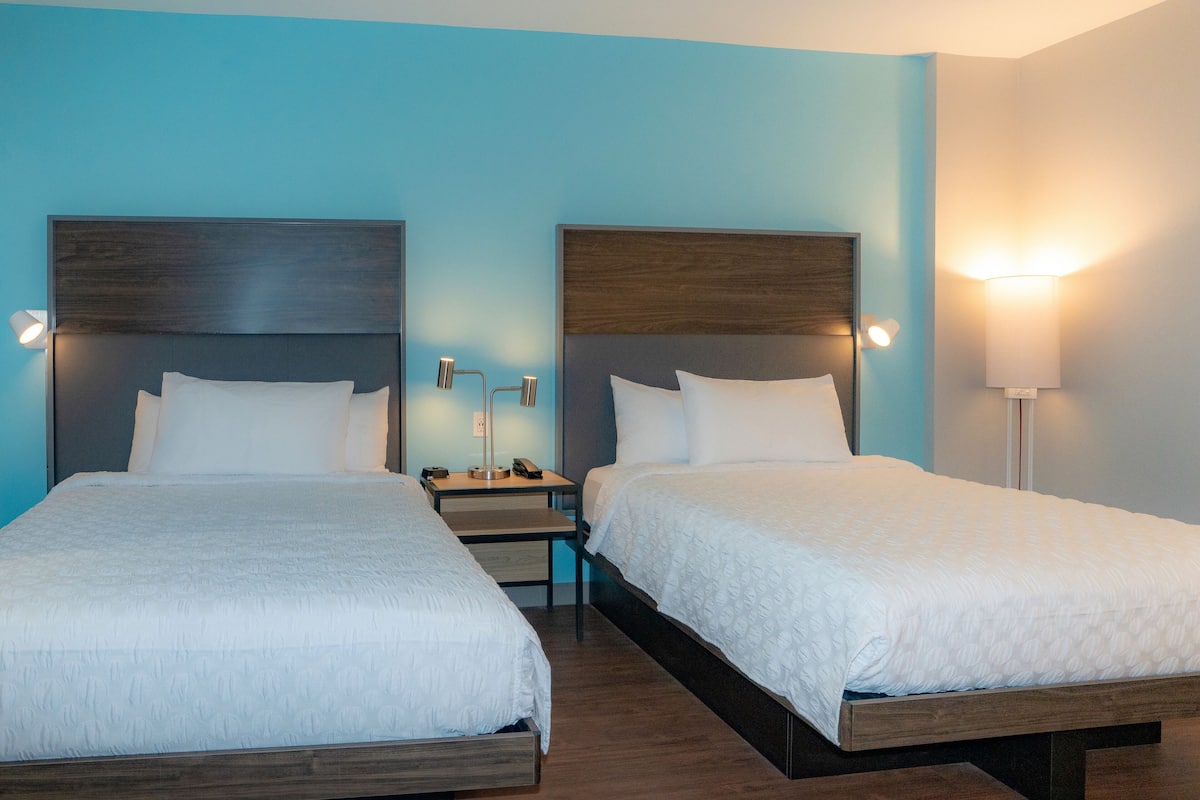 Une chambre d’hôtel avec deux lits, une table de chevet et une petite table de nuit avec une lampe.