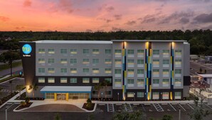 A modern hotel building with a prominent Hilton logo, multiple floors, and a parking lot. - Tru by Hilton Jacksonville Airport I-95 (Jacksonville)