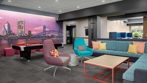 A modern lounge area with a pool table, comfortable seating, and a cityscape mural on the wall. - Tru by Hilton Jacksonville Airport I-95 (Jacksonville)