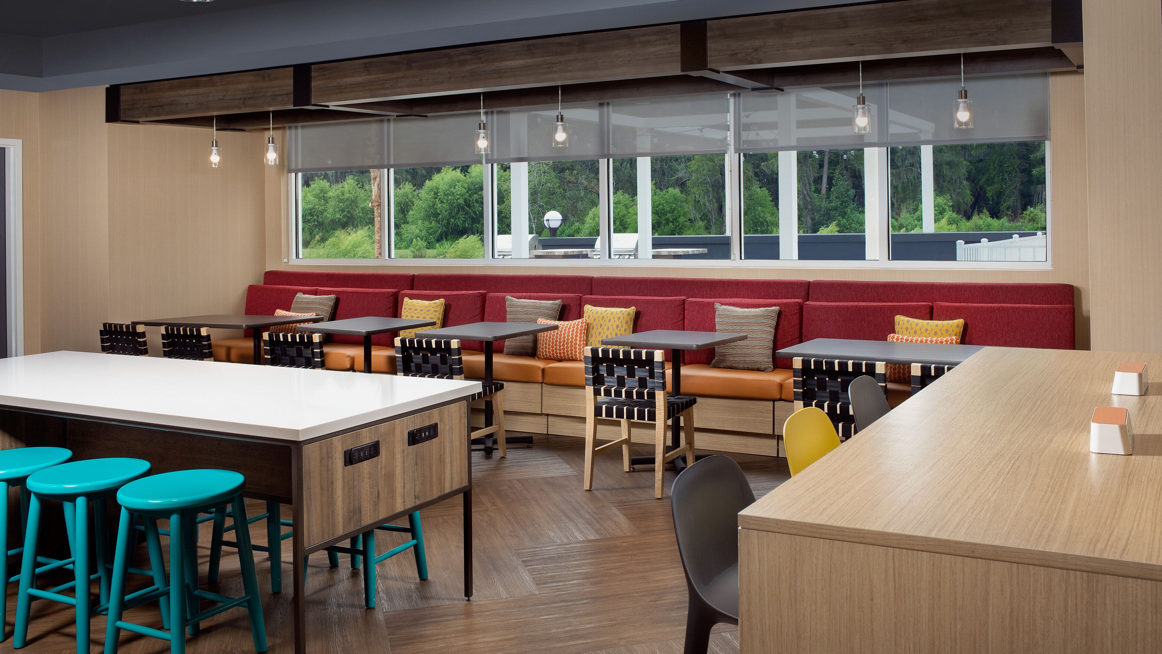 A modern cafe with wooden tables, colorful chairs, and a red cushioned bench.