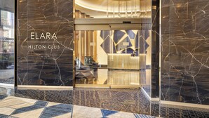 La entrada del Elara Hilton Club, con un diseño moderno, que presenta una fachada de mármol y un suelo con estampado geométrico.