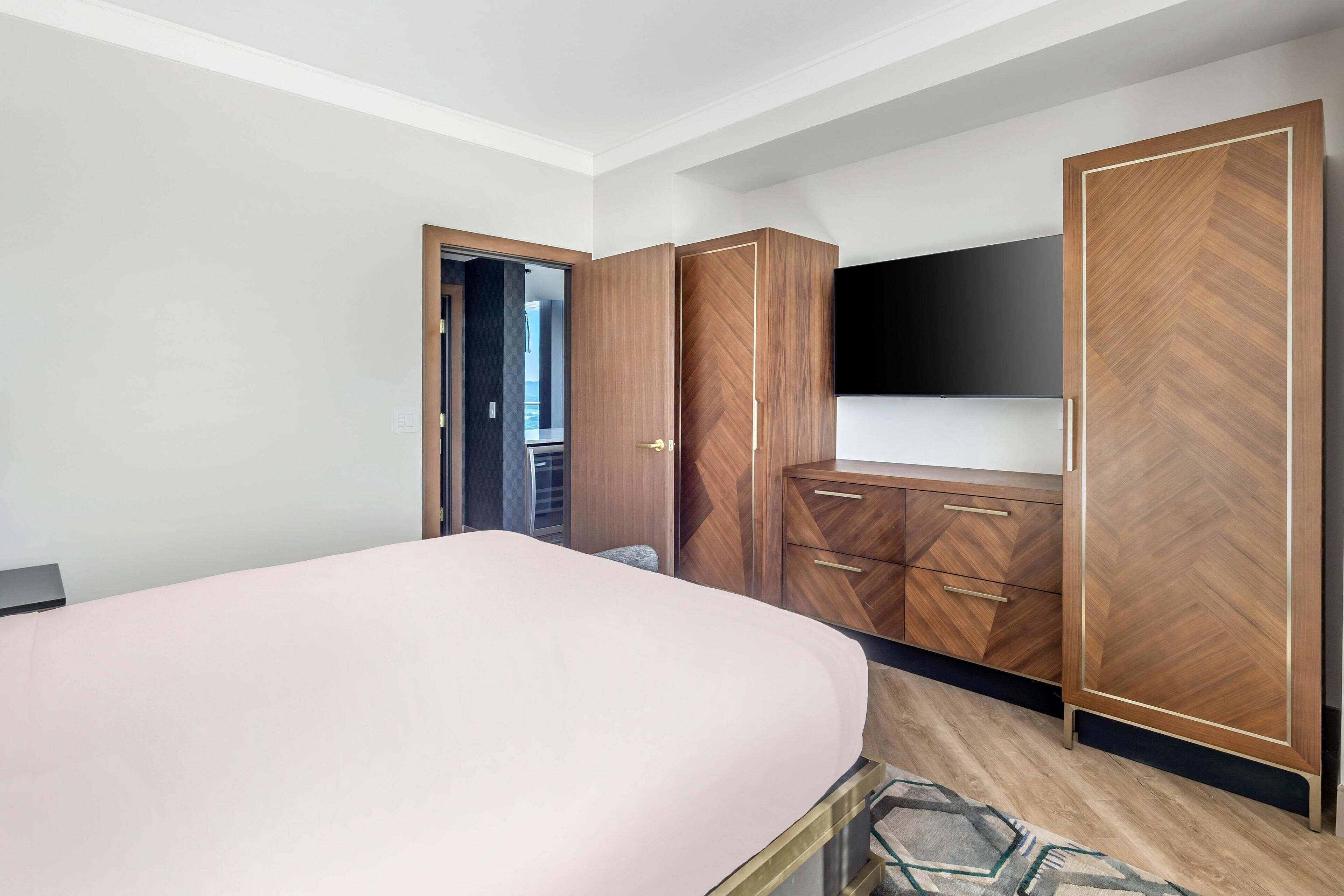 Un dormitorio con cama, armario de madera y televisión en la pared.