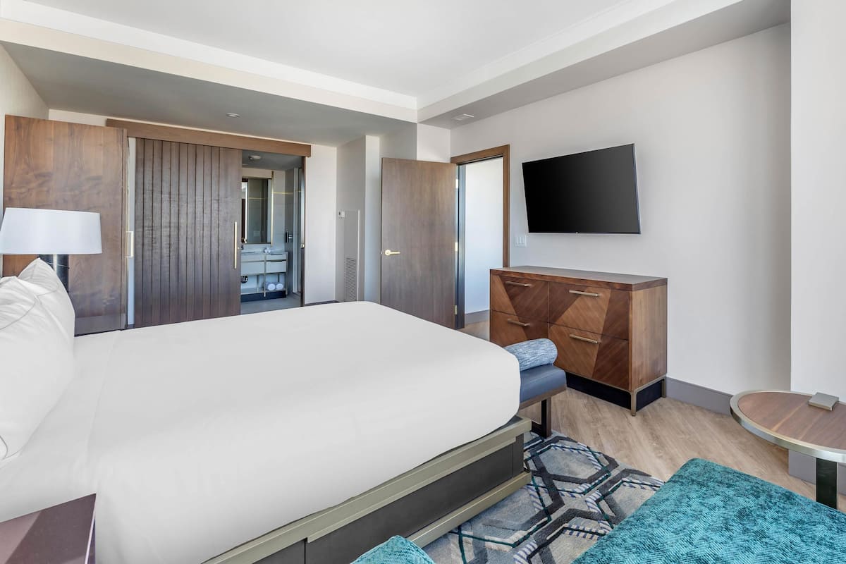 Une chambre d’hôtel moderne avec un grand lit, un téléviseur à écran plat, une commode en bois et une petite table.