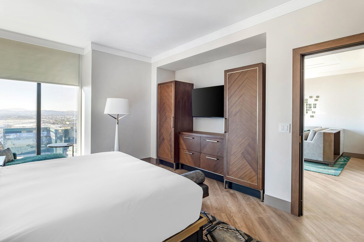 A hotel room with a large bed, a TV, wooden wardrobe, and a city view.