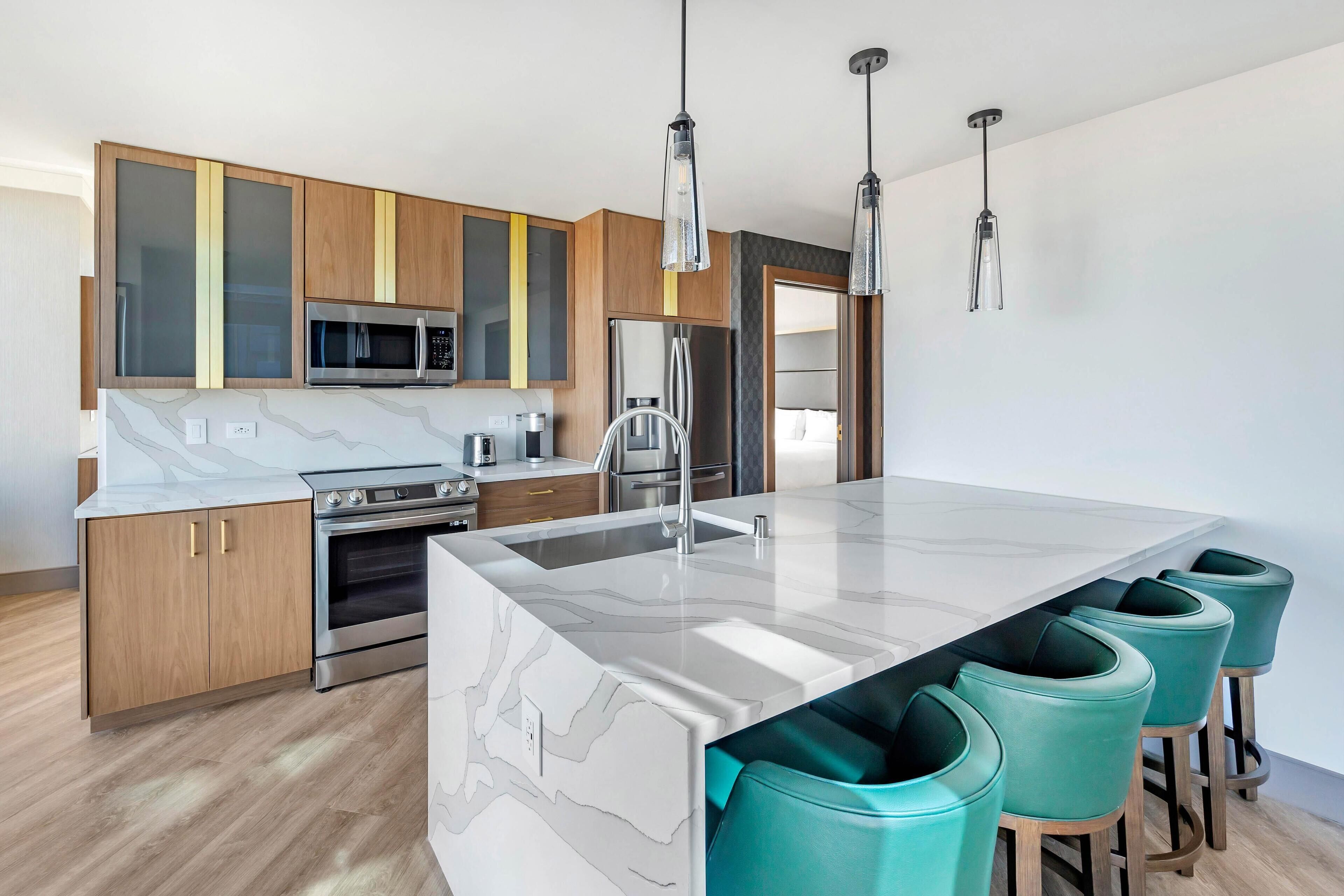 A modern kitchen with a marble island, stainless steel appliances, and teal bar stools.