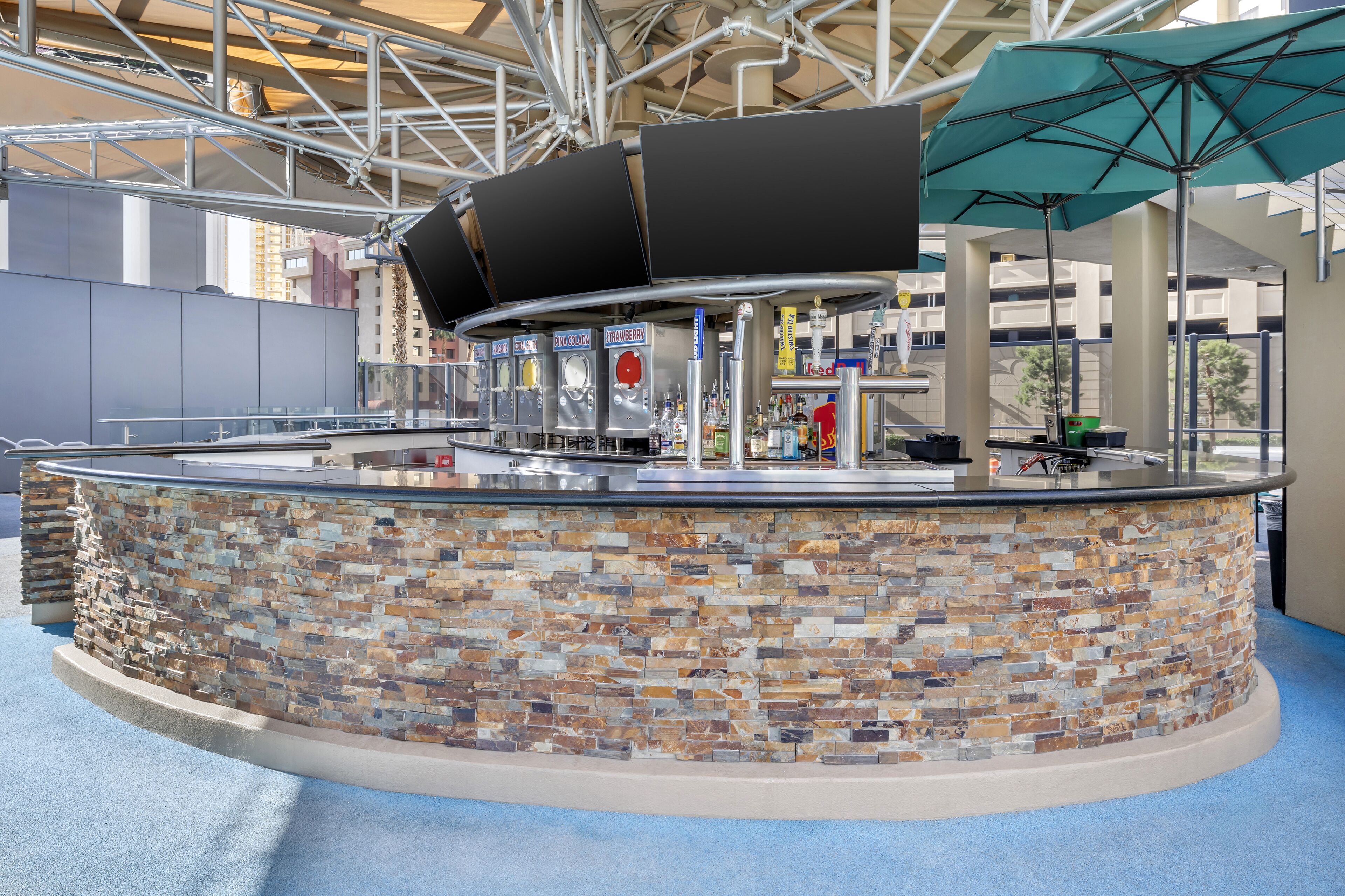 A bar area with a stone wall, multiple drink dispensers, and a large umbrella.