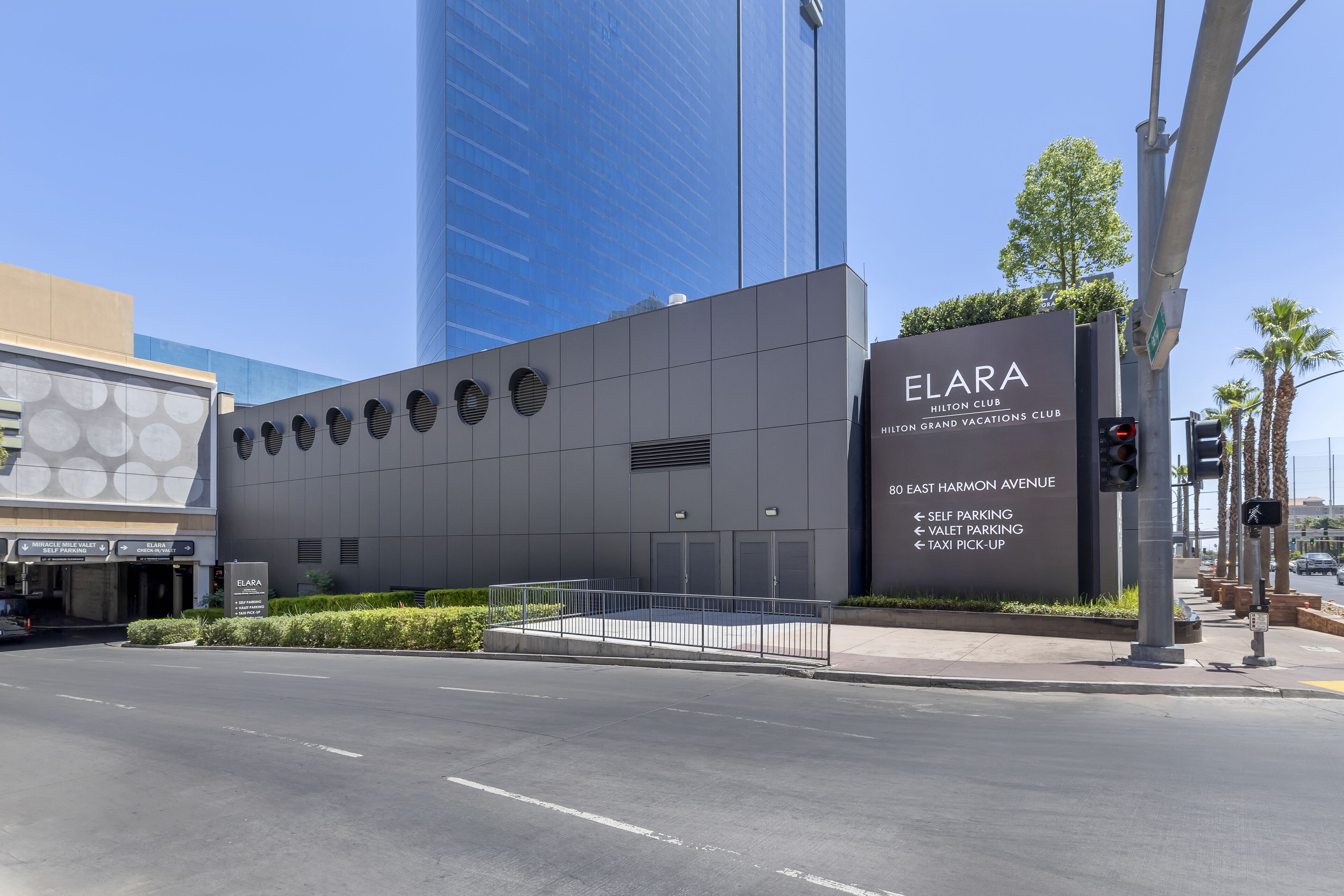 A modern building with a sign for ELARA Hilton Club, indicating self parking, valet parking, and taxi pick-up services.