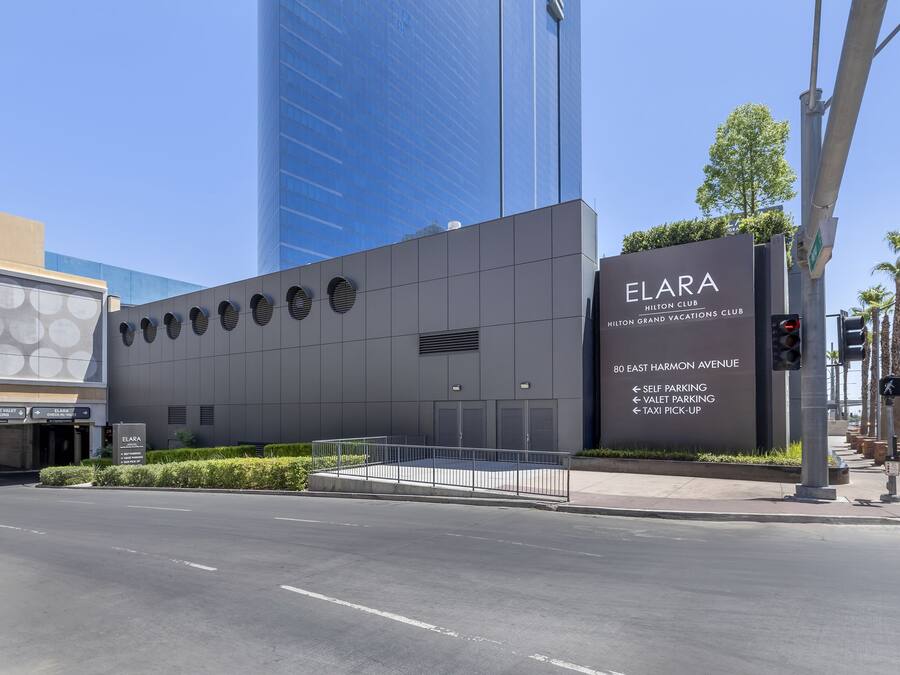 A modern building with a sign for ELARA Hilton Club, indicating self parking, valet parking, and taxi pick-up services.