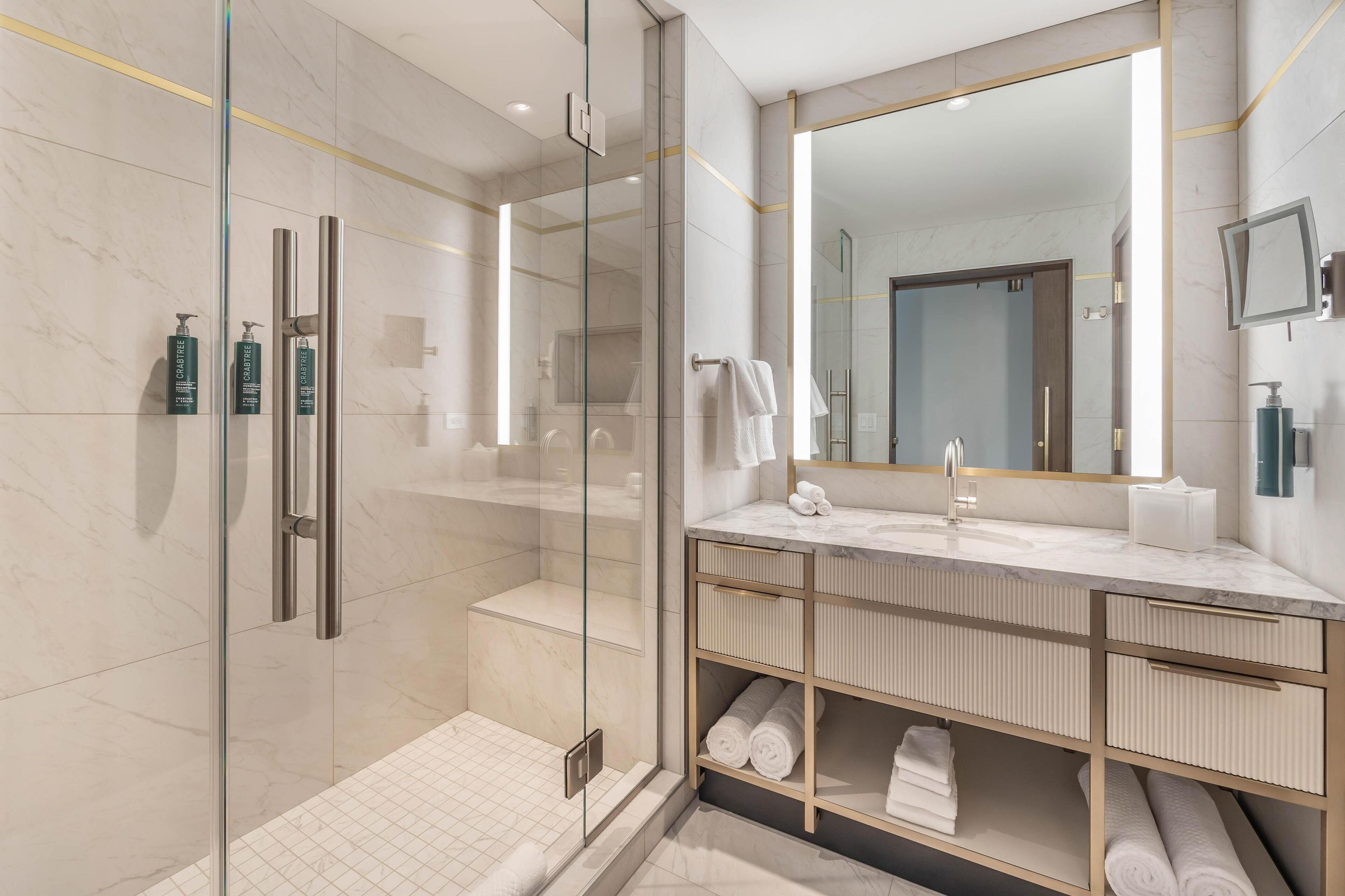 Un baño moderno con ducha de vidrio, un espejo grande y un tocador con espacio de almacenamiento.