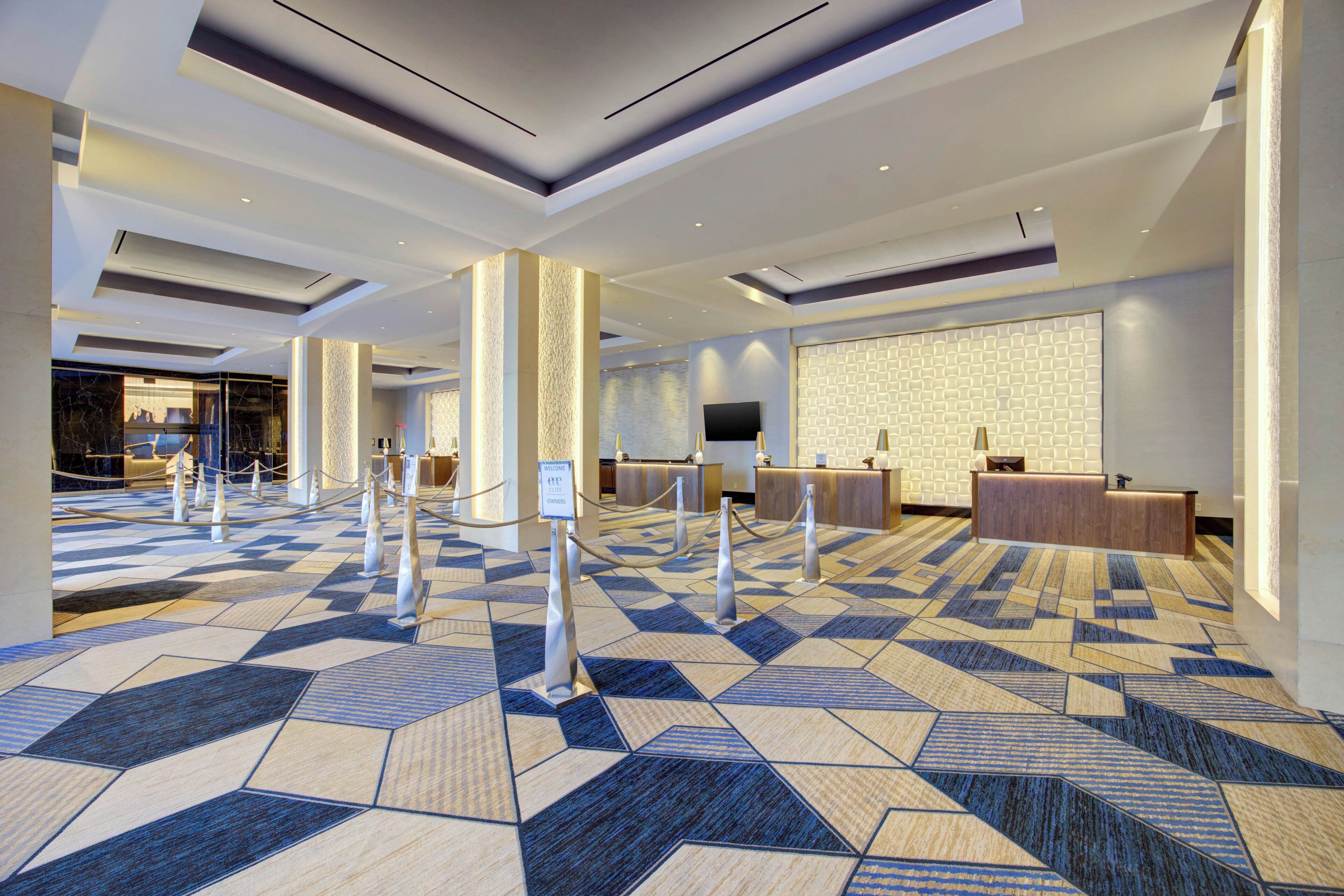 Un'hall dell'hotel con una moquette a motivi geometrici, una reception e un grande schermo a parete.
