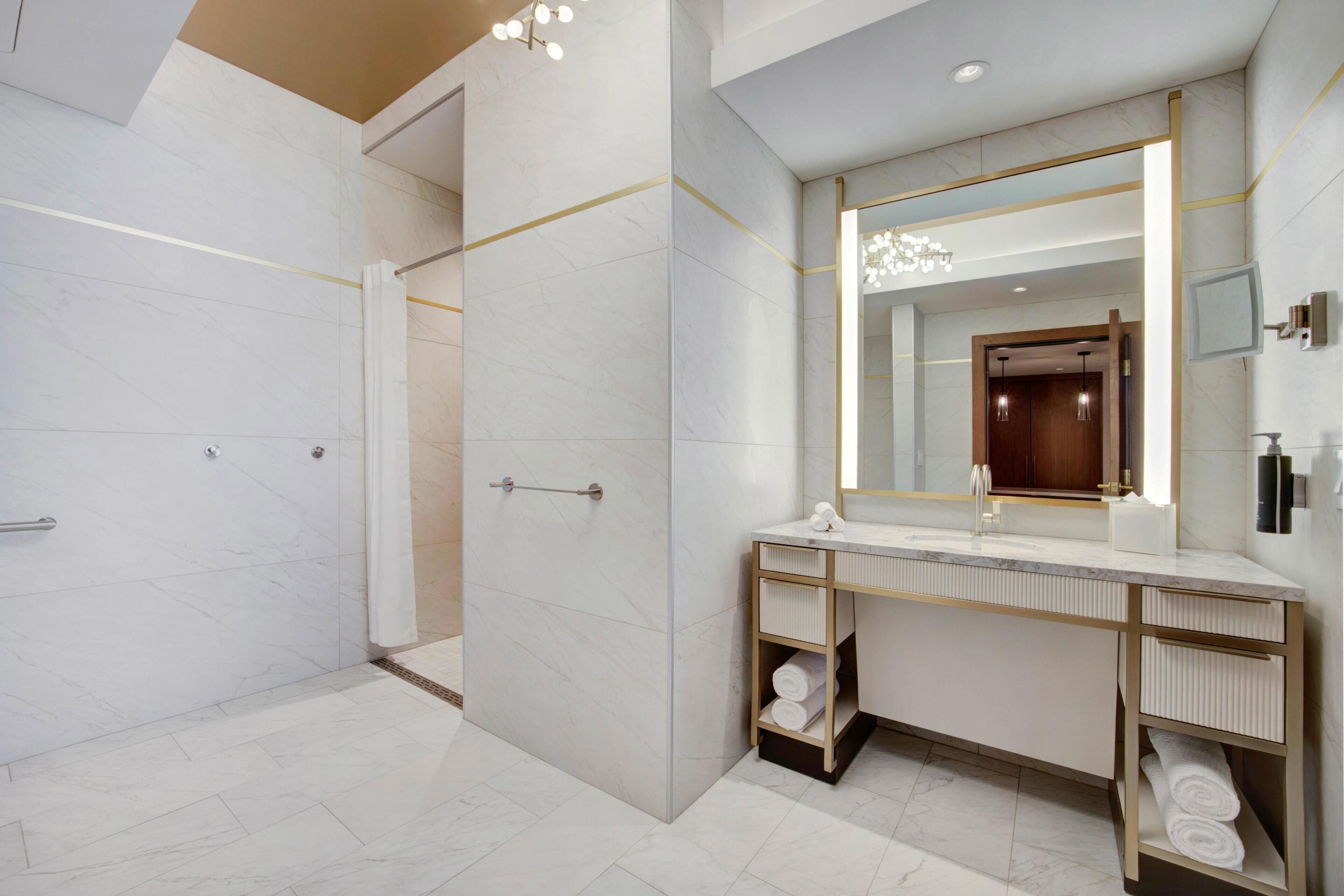 A modern bathroom with a walk-in shower, a large mirror, and a vanity with a towel rack.