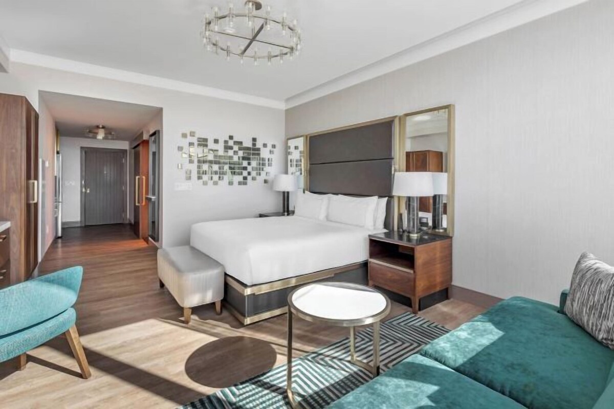 A hotel room with a large bed, a desk, a chair, a sofa, and a mirror.
