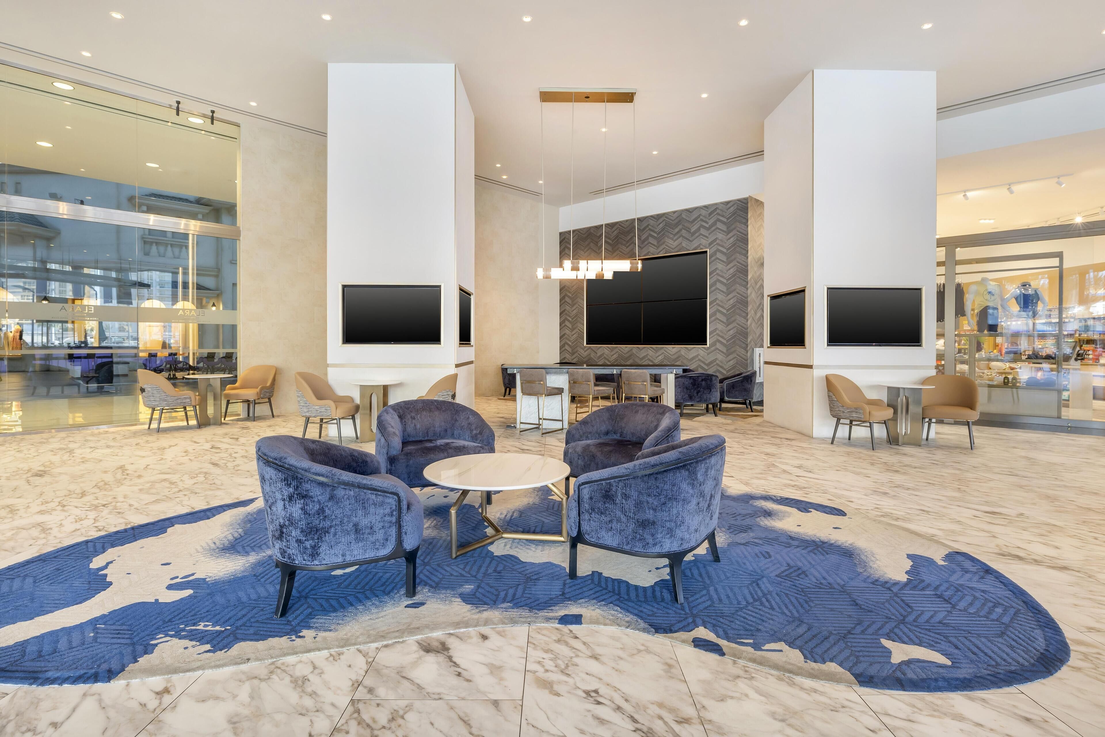 A modern lobby with seating, a large TV screen, and a patterned carpet.