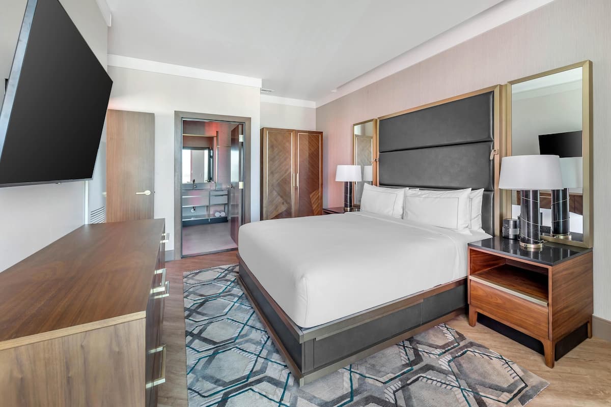 Une chambre d’hôtel moderne avec un grand lit, une table de chevet en bois, une télévision et un miroir.