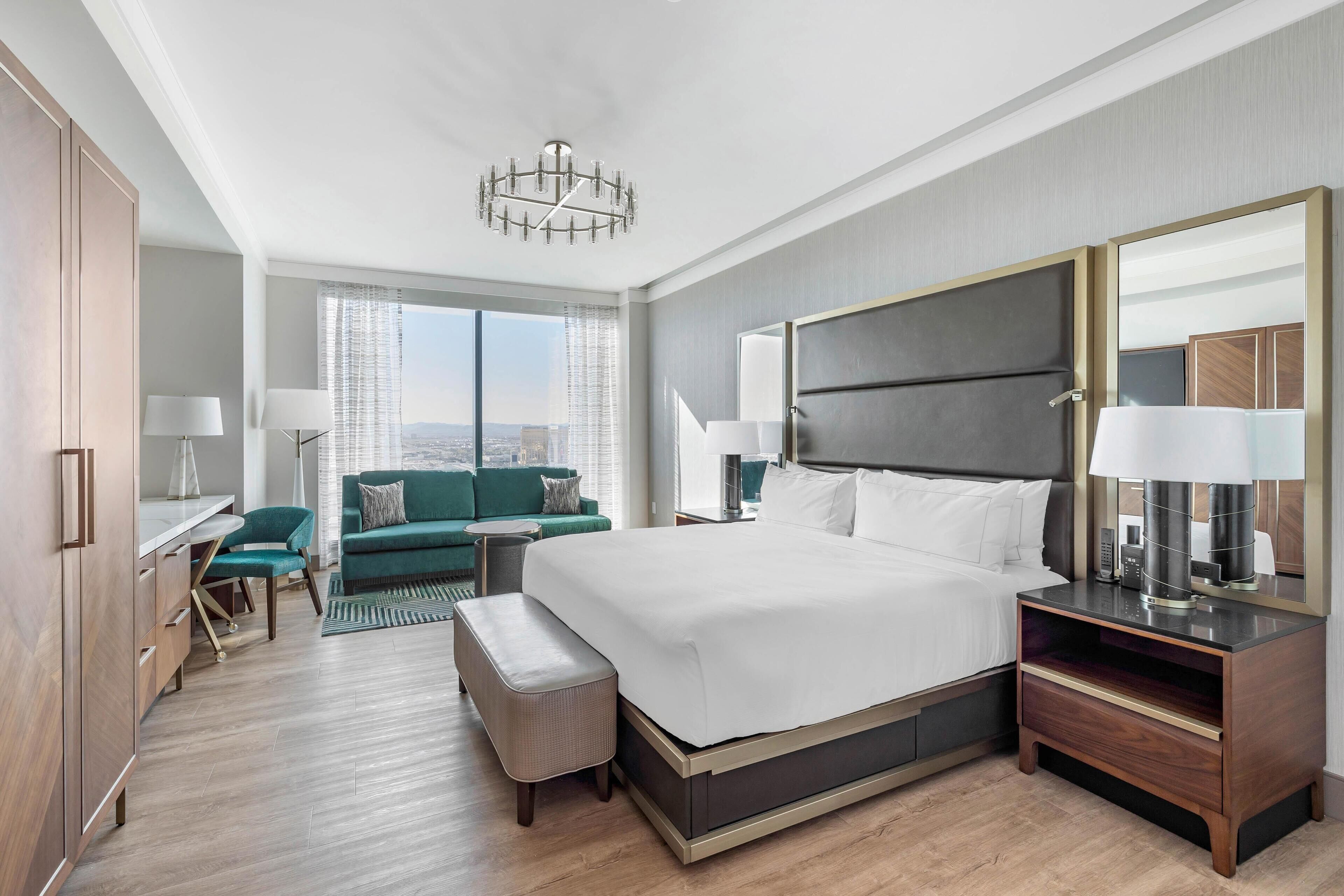 Een moderne hotelkamer met een groot bed, een bureau, een groene bank en uitzicht op de stad.