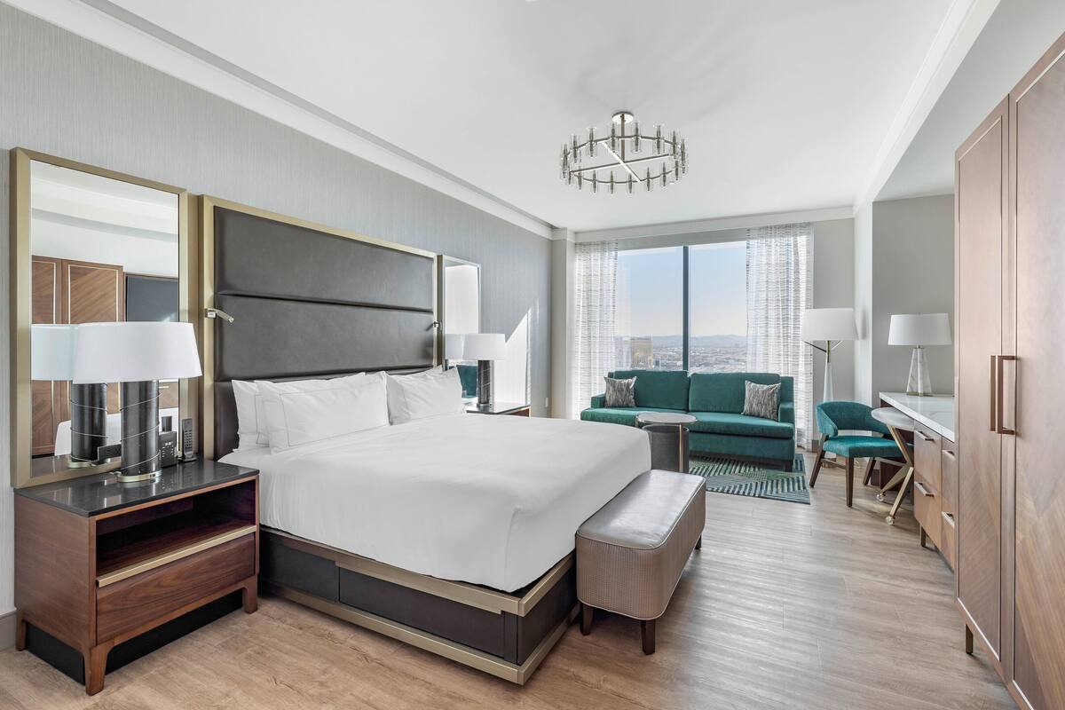 Une chambre d’hôtel moderne avec un grand lit, un bureau, un canapé vert et une vue sur la ville.