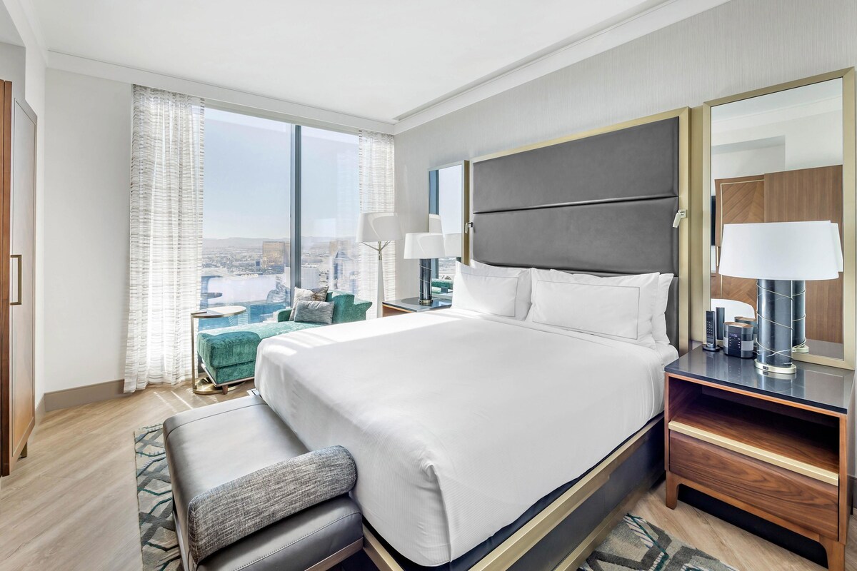 A modern hotel room with a large bed, a seating area, and a view of the city.