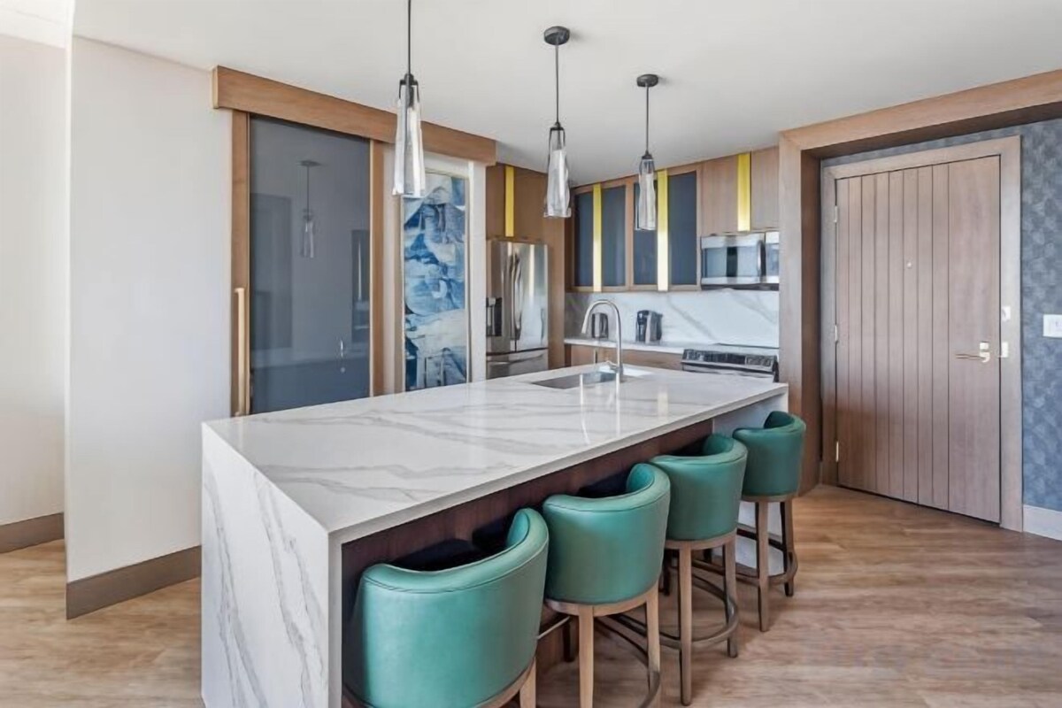 A modern kitchen with a marble island, bar stools, pendant lights, and a microwave.