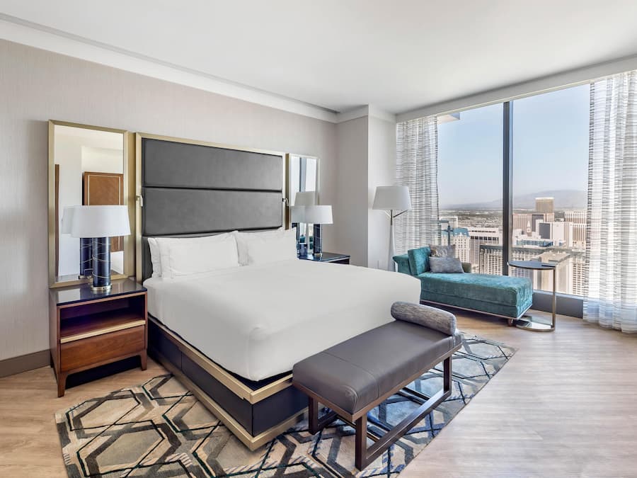 Ein modernes Hotelzimmer mit einem großen Bett, einer Bank, einem kleinen Sofa und Blick auf die Stadt.