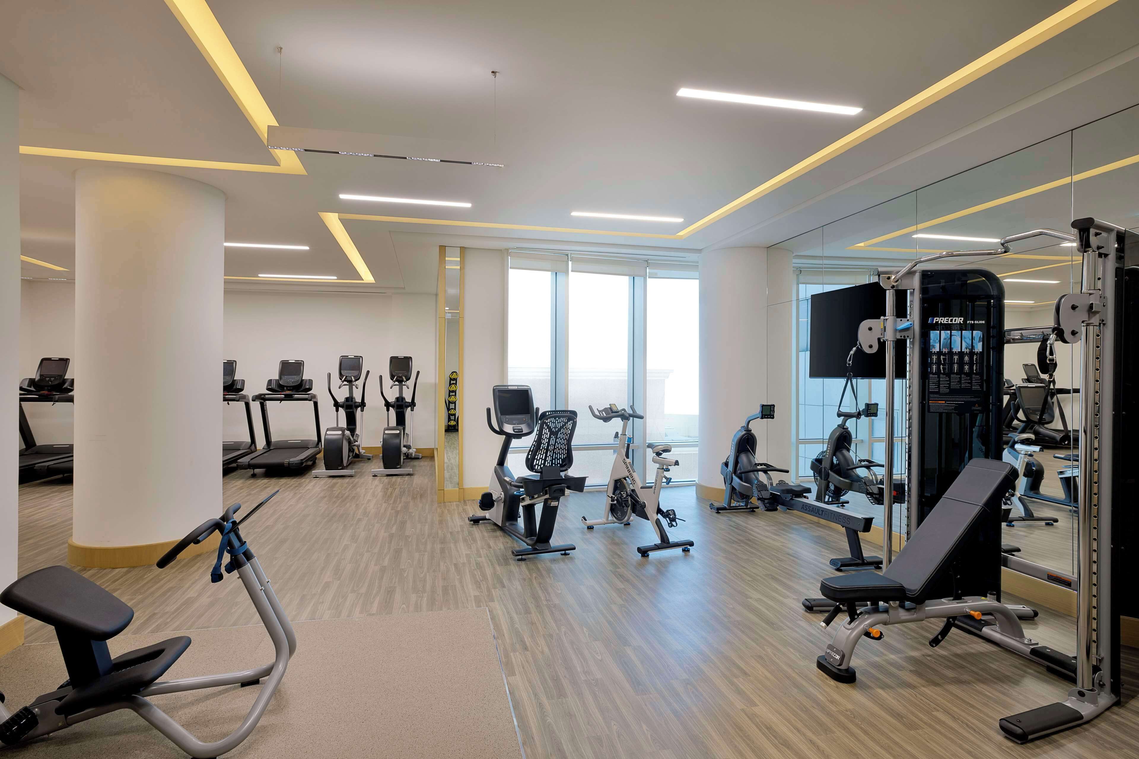 Et moderne fitnesscenter med forskellig træningsudstyr, store vinduer og en lys, rummelig indretning.