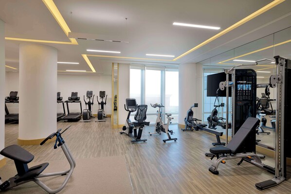 A modern gym with various exercise equipment, large windows, and a clean, spacious layout.