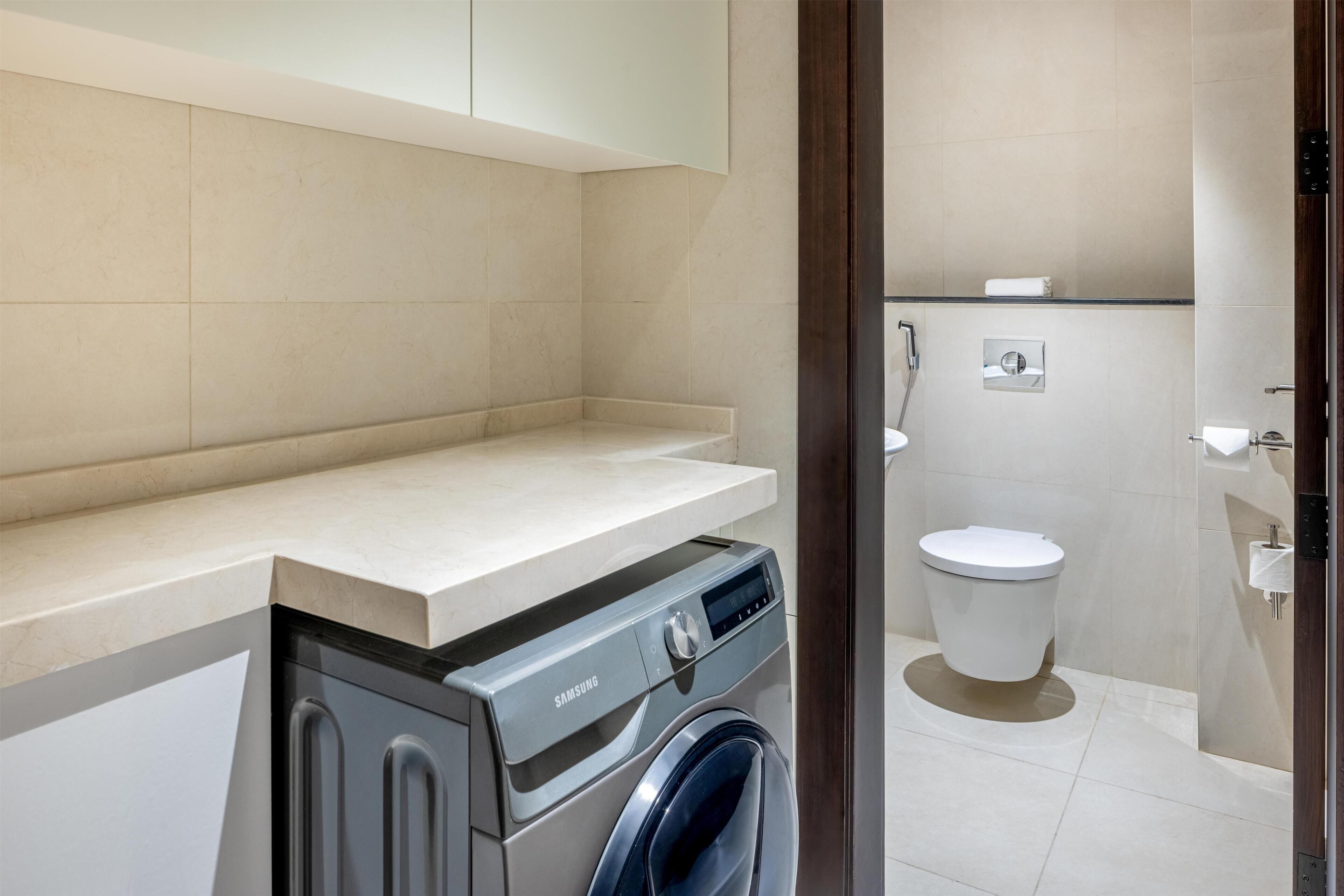 A modern bathroom with a washing machine, toilet, and a shower area.