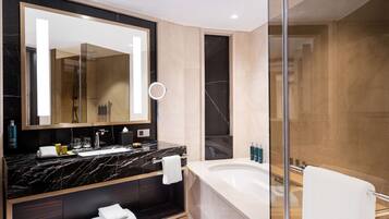 A modern bathroom with a large mirror, a black marble vanity, a bathtub, and a glass shower enclosure.