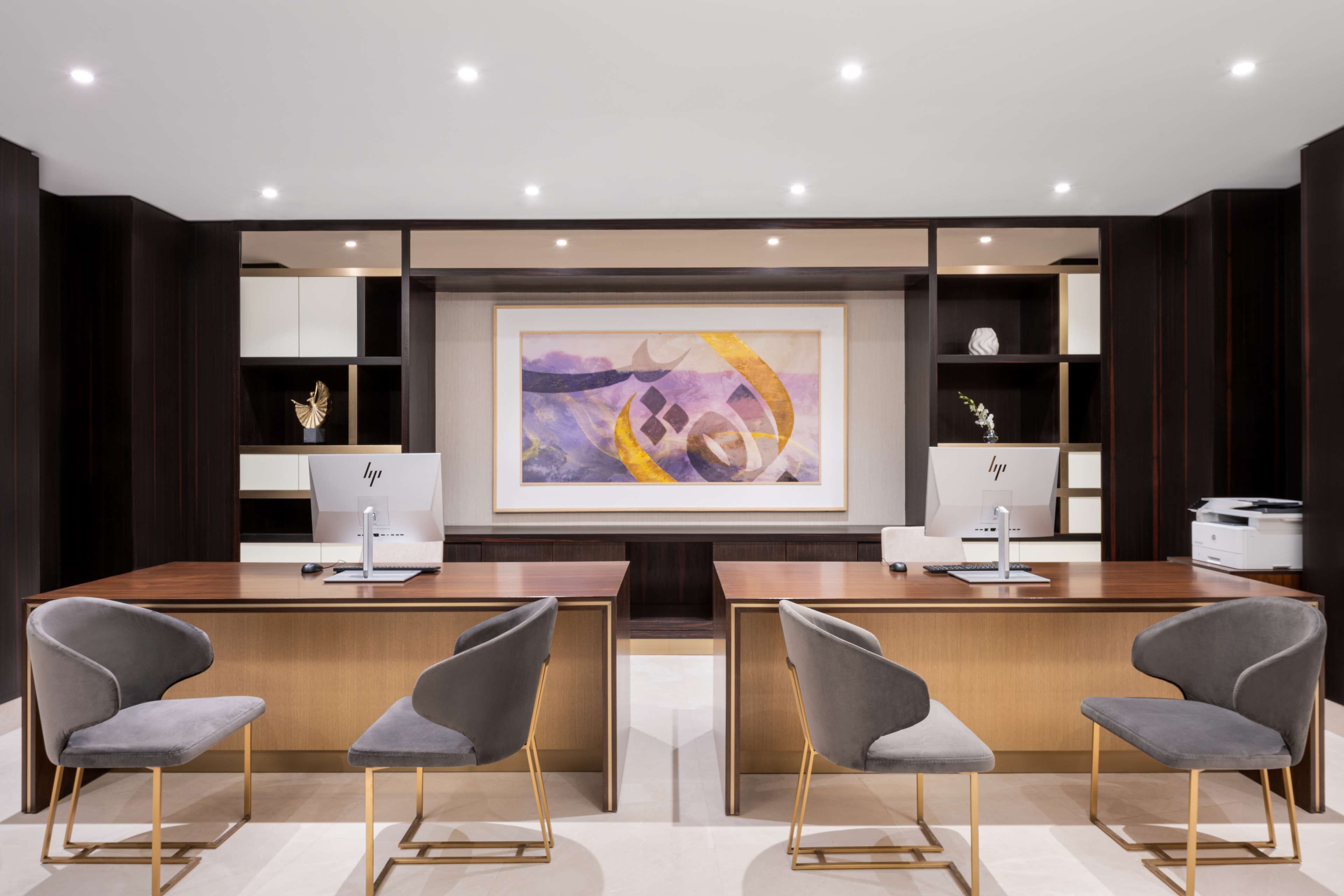 A modern office space with two desks, two chairs, a large abstract painting, and shelves with decorative items.