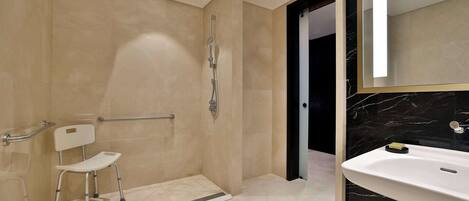 A modern bathroom with a walk-in shower, a white pedestal sink, and a large mirror.