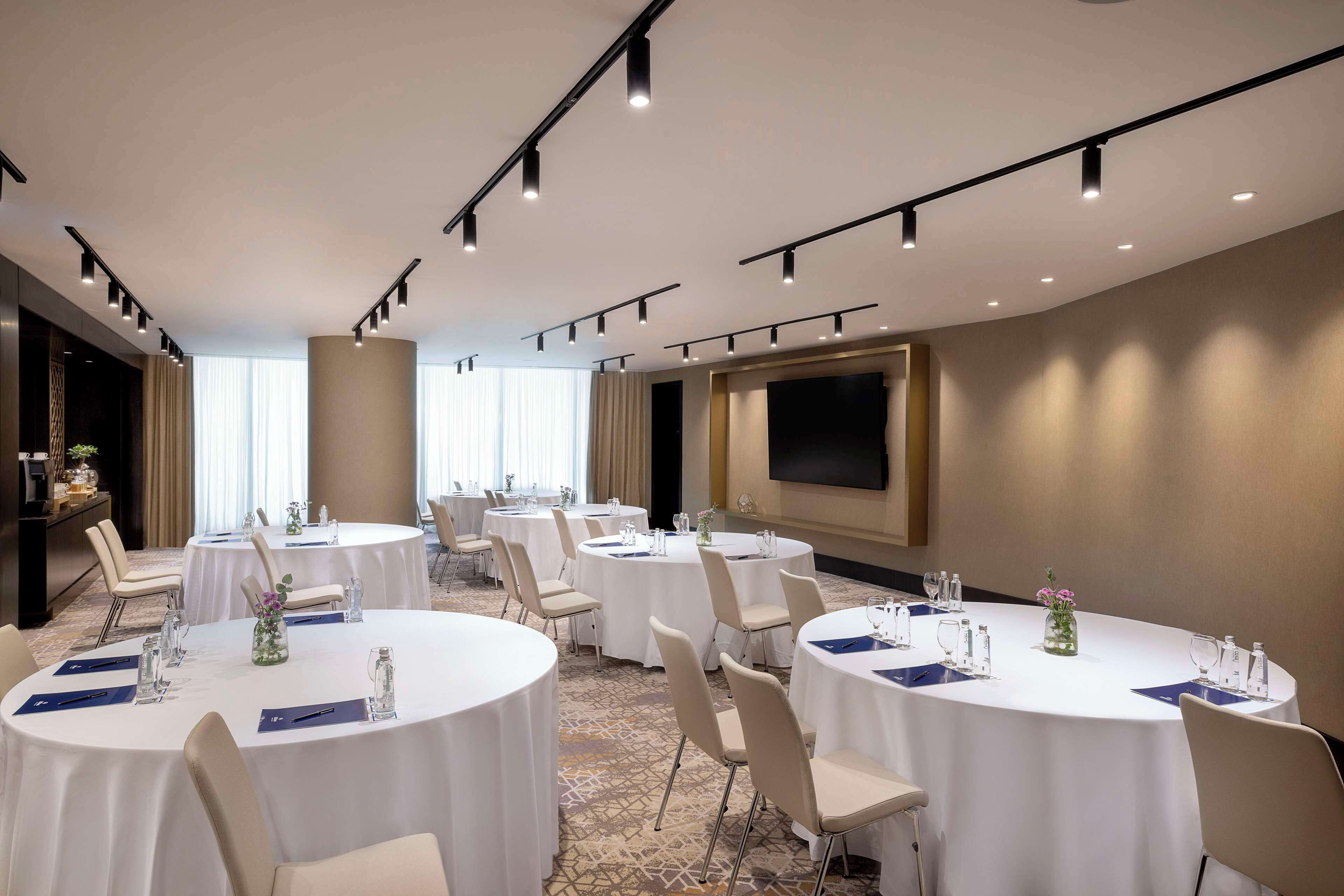 A conference room with round tables, chairs, and a large screen.