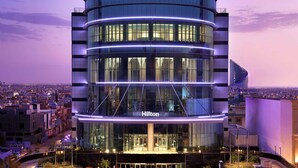 A modern Hilton hotel with a curved glass facade, multiple floors, and a prominent entrance. - Hilton Riyadh Olaya (Riyadh)