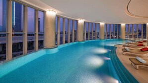 A large indoor swimming pool with a city view, multiple lounge areas, and a modern architectural design. - Hilton Riyadh Olaya (Riyadh)